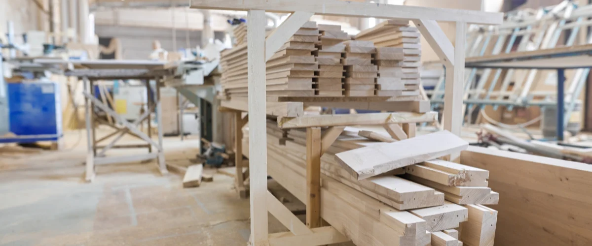 Stacks of light-colored sawn timber and wood planks on wooden racks in a blurred carpentry workshop. Stacks of light-colored sawn timber and wood planks on wooden racks in a blurred carpentry workshop.