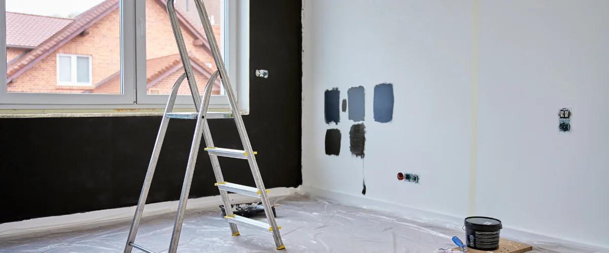 A partially painted room with a ladder, black wall, white walls with paint swatches, and a paint can.