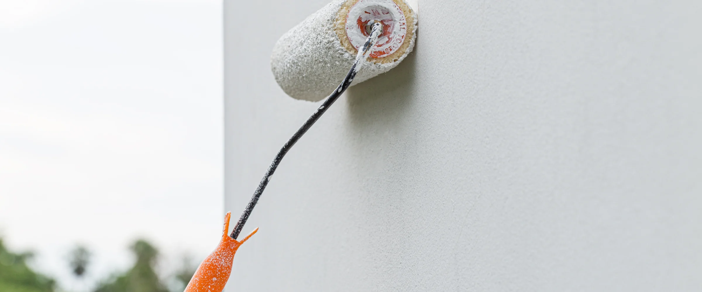 Close-up of a man in a cap and gloves painting an exterior window trim with a paintbrush.