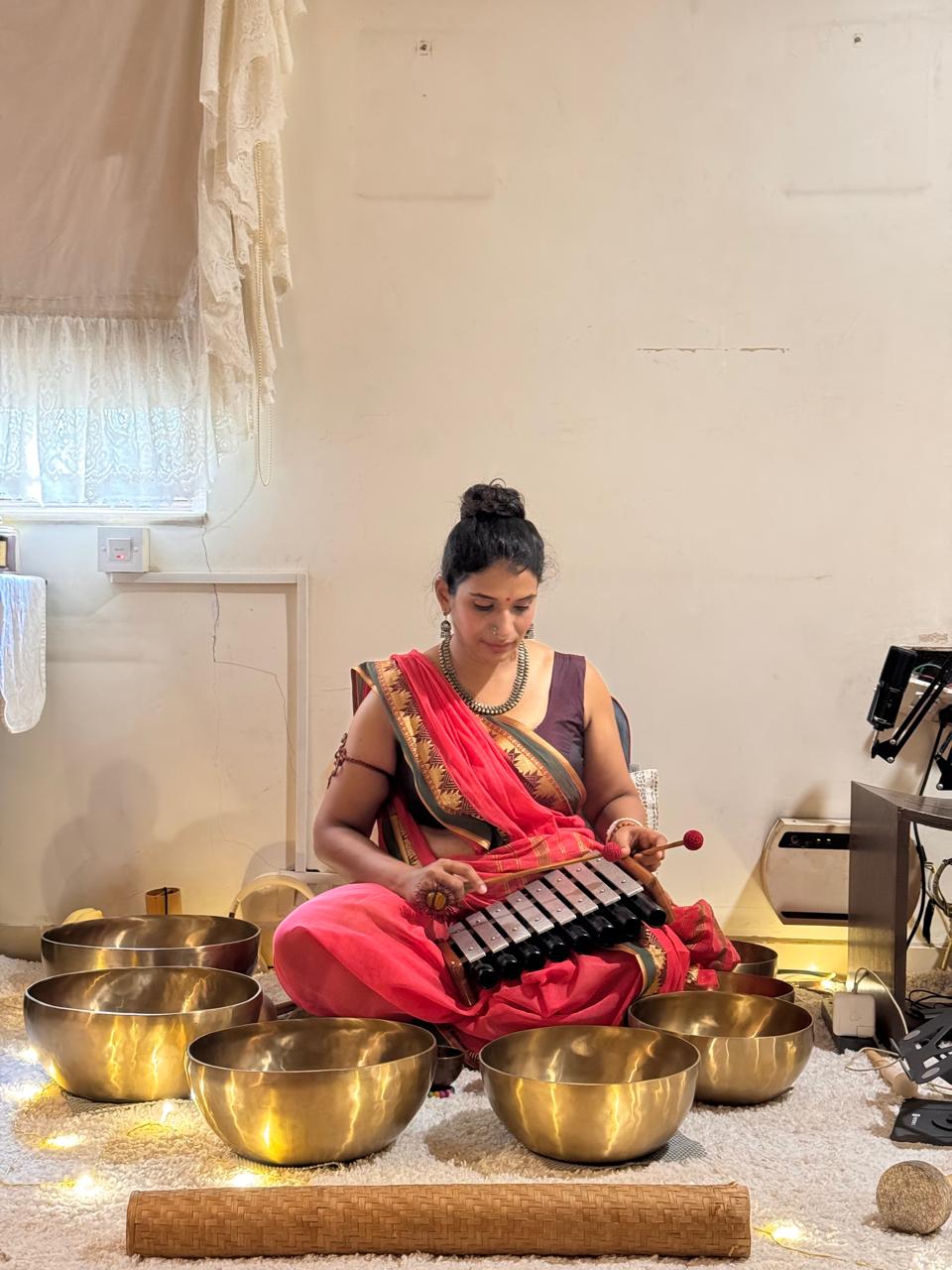 A facilitator playing a metallophone, surrounded by brass singing bowls