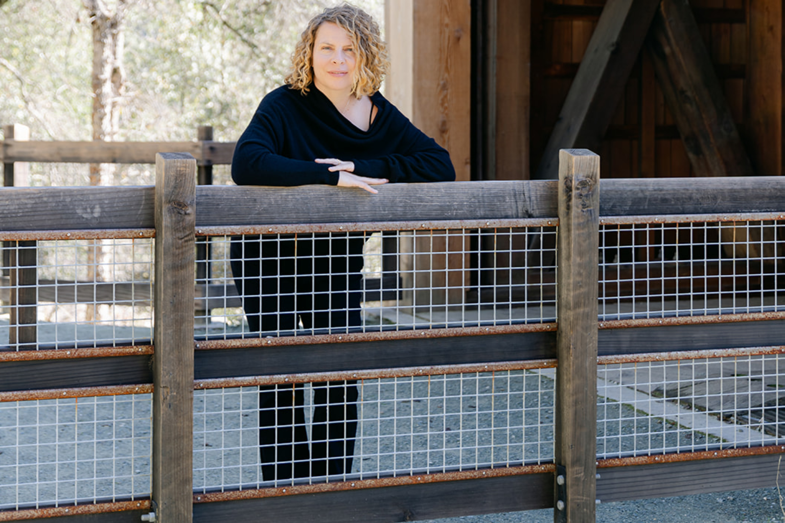Radha Heartwell standing at a wood and wire fence rail, looking out