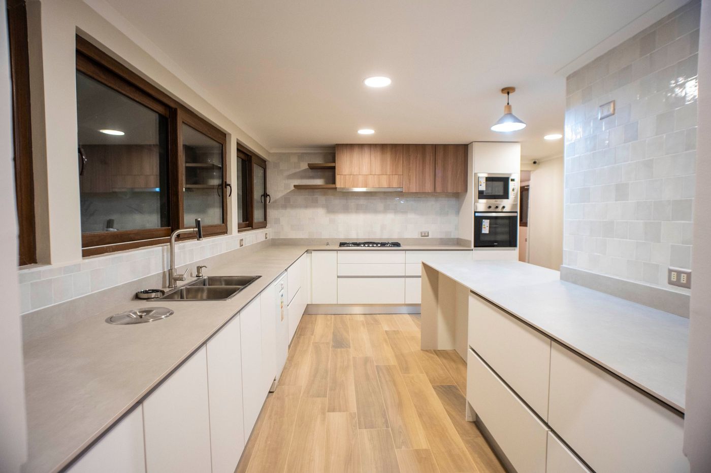 Cocina remodelada de Casa Arrayán con muebles blancos, cubierta gris, muebles altos de madera y piso tipo madera