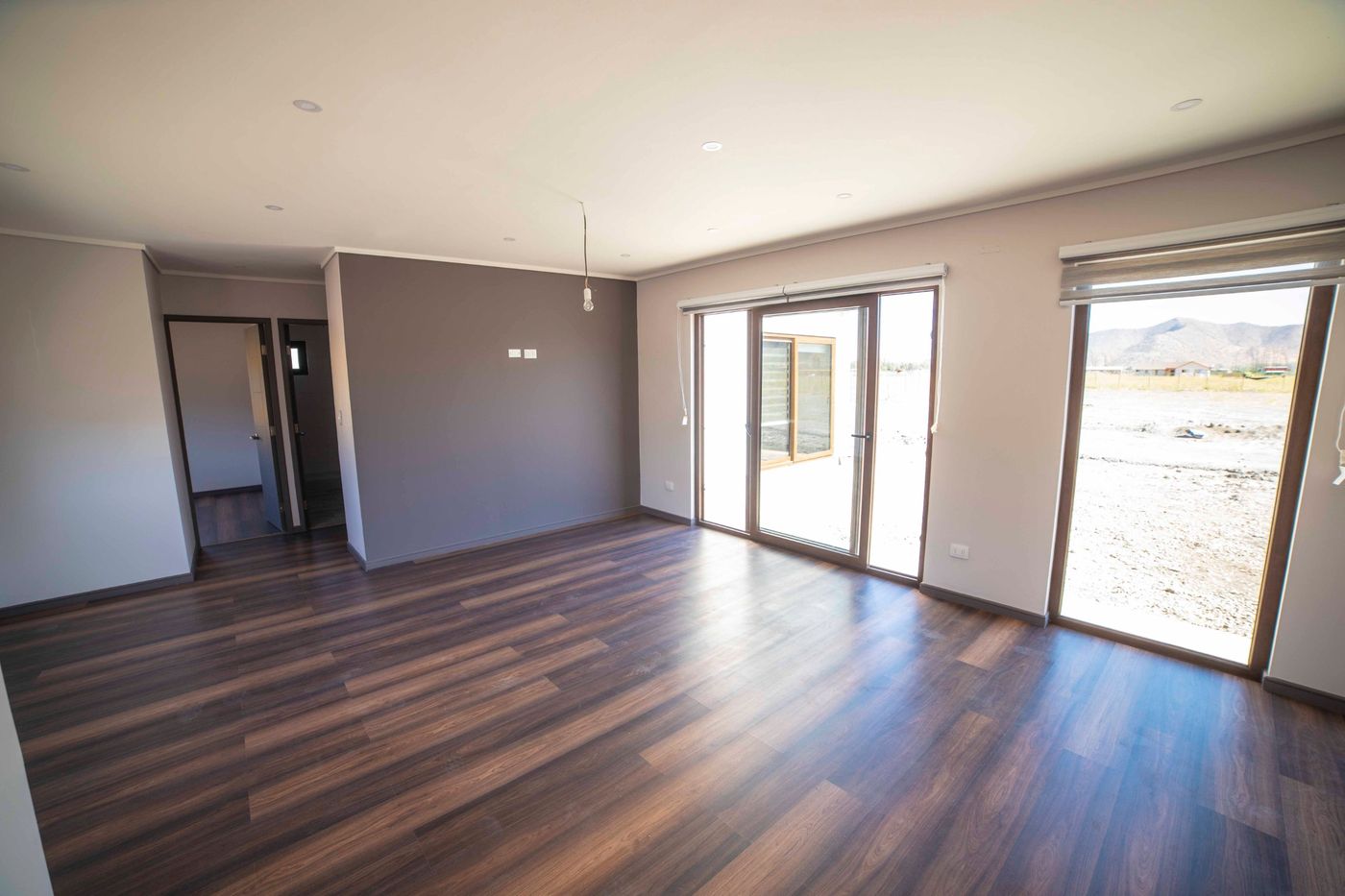 Living de la casa nueva con piso flotante oscuro, ventanales corredera y vista a los cerros
