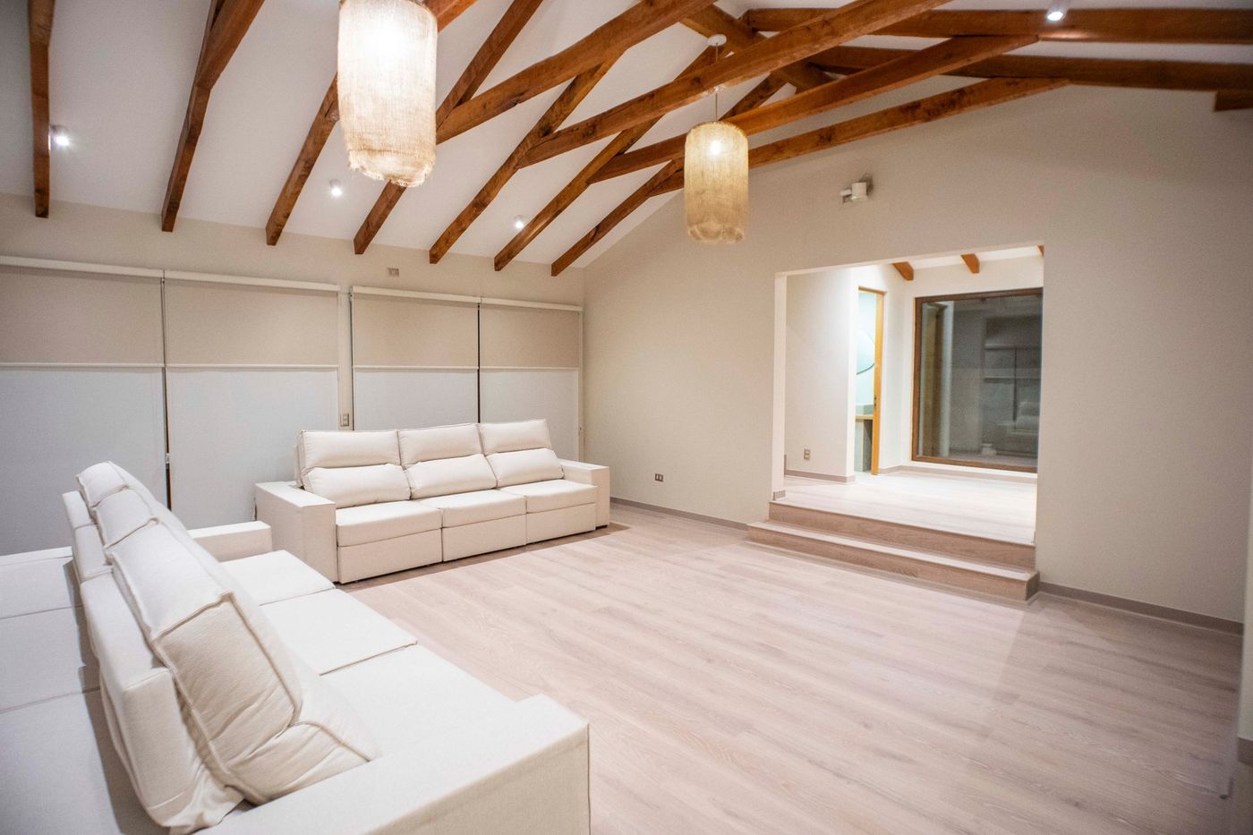 Living de Casa Arrayán con vigas de madera conservadas, sofás blancos y piso nuevo
