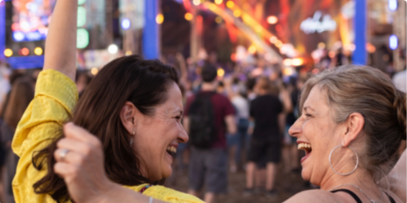 Two women over 50 laughing and enjoying a music festival together in the UK Two women over 50 laughing and enjoying a music festival together in the UK