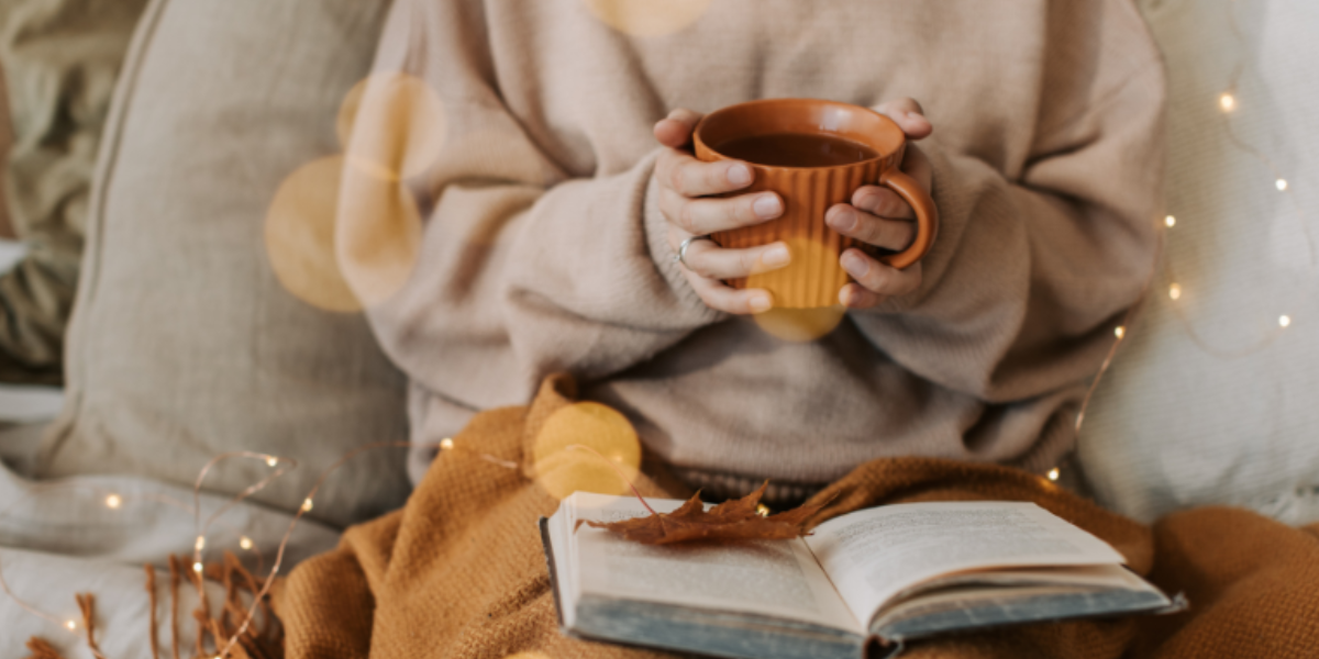 Woman holding a hot drink with a book on her lap Woman holding a hot drink with a book on her lap