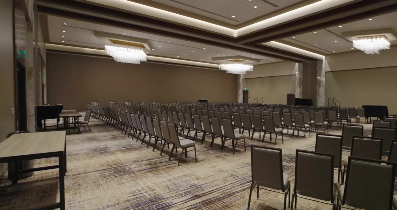 Large ballroom with rows of chairs, chandeliers, and patterned carpet