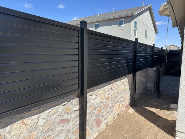 Black horizontal metal fence on top of rock wall