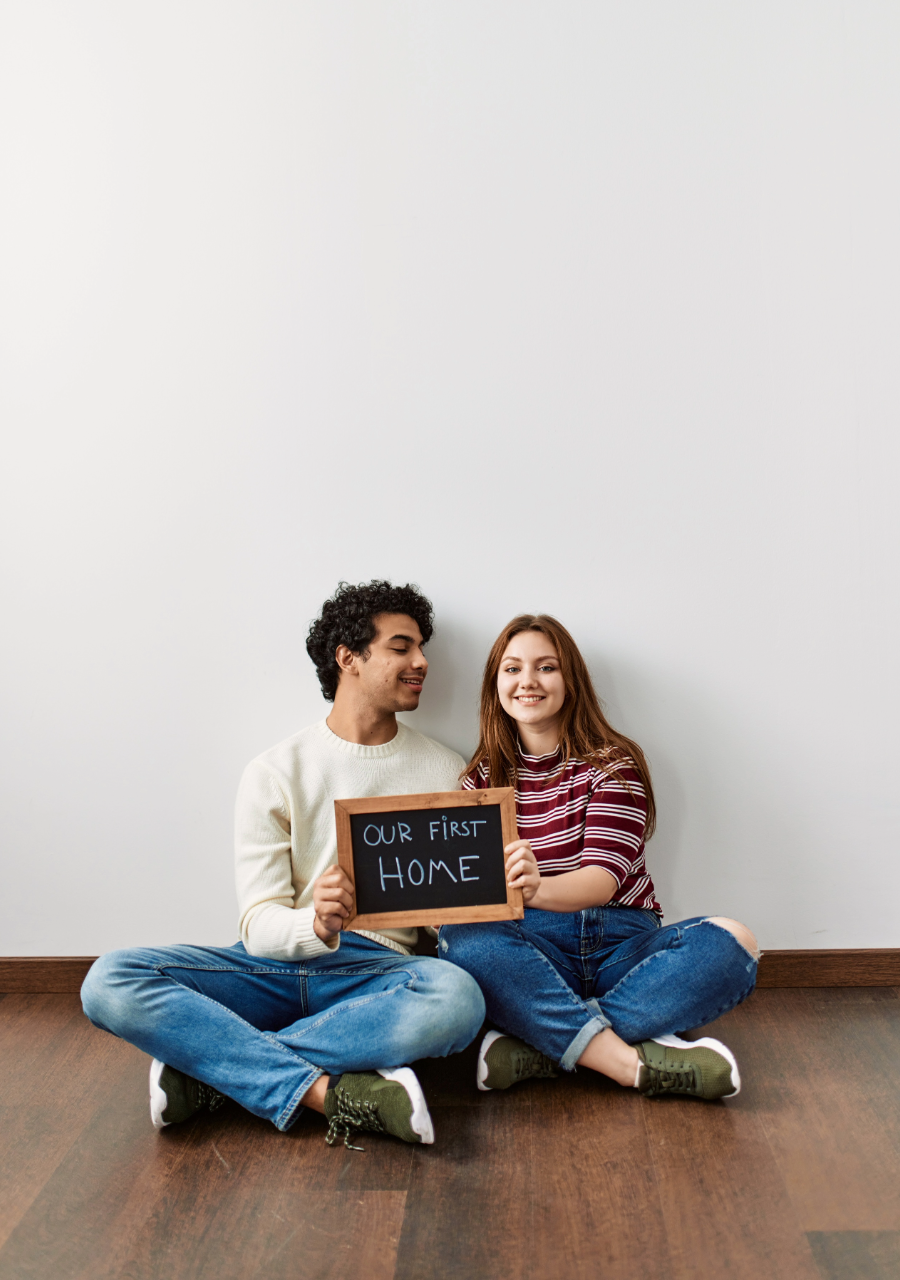 Simplicity — couple sitting with Our First Home sign