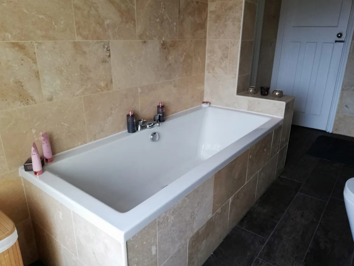 Double-ended white bath with a tiled panel and travertine-effect wall tiles