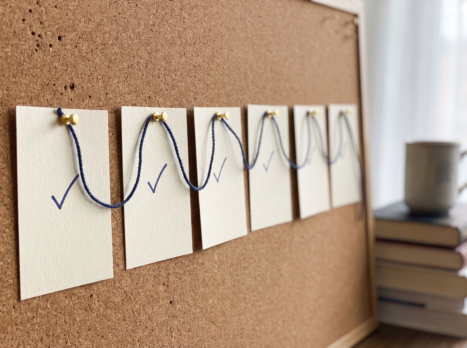 Six index cards pinned in a row and joined by string, each with a check mark