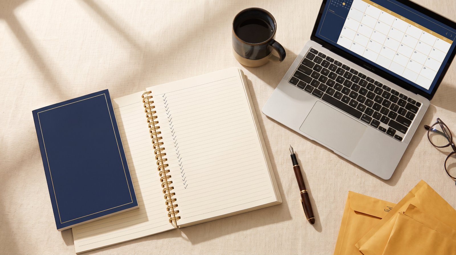 A finished paperback, an open planning workbook and a laptop showing a launch calendar on a writer's desk