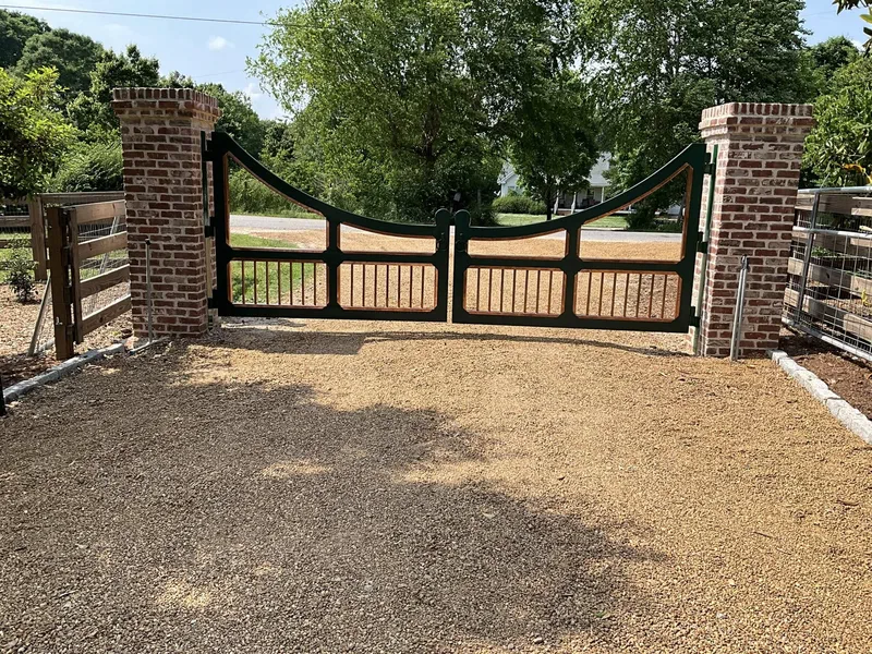 Black metal driveway gate hung between brick columns