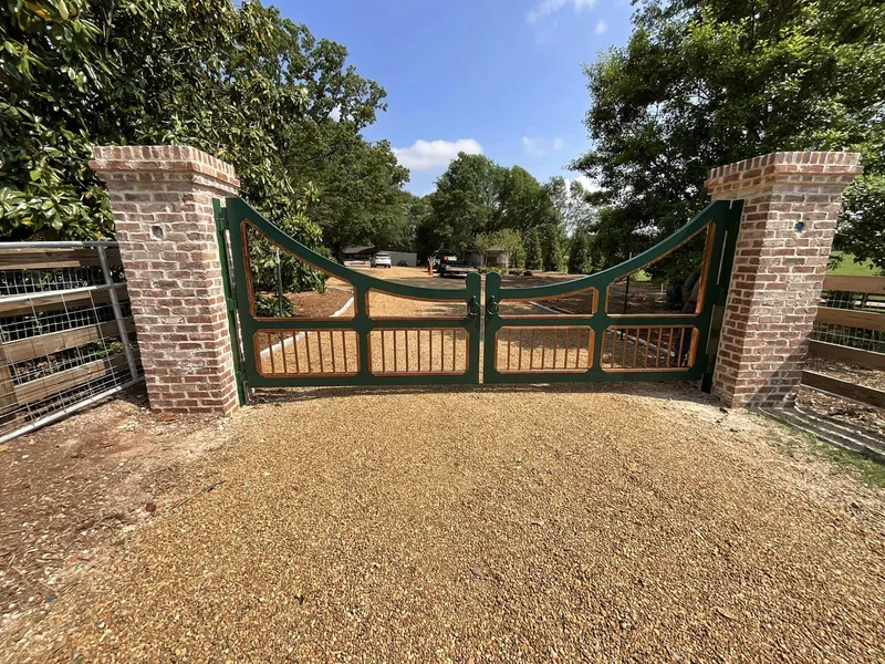 Green metal driveway gate hung between brick columns