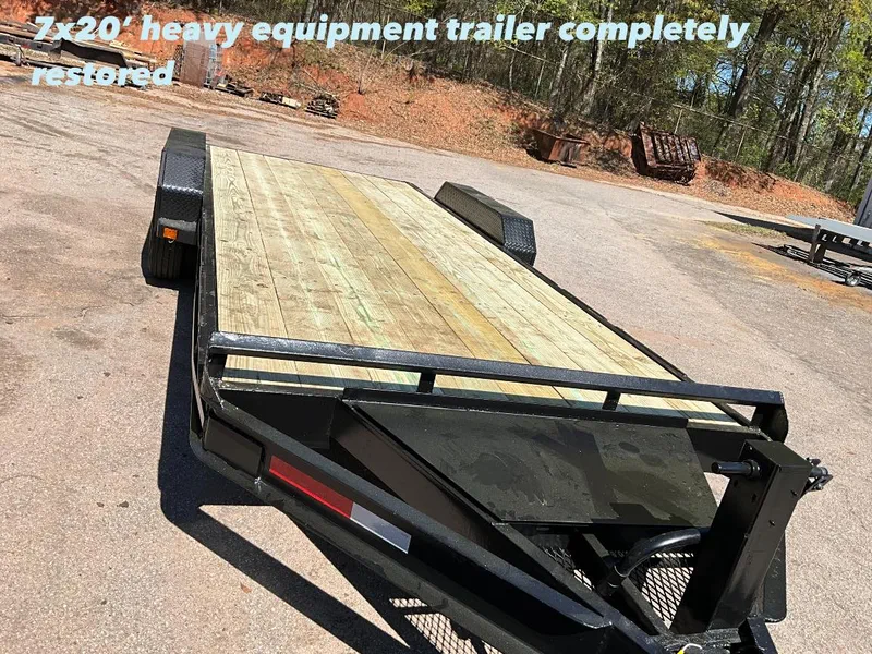 Heavy equipment trailer with a timber deck and fold-down ramps