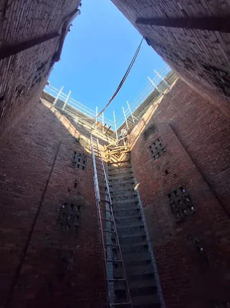 Steel stair tower rising inside an open brick shaft toward the sky
