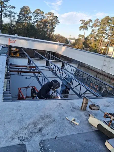 Welder working on steel roof framing above an open structure