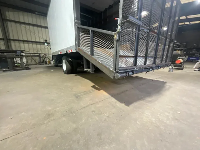 Equipment trailer with its mesh loading ramp raised in the shop