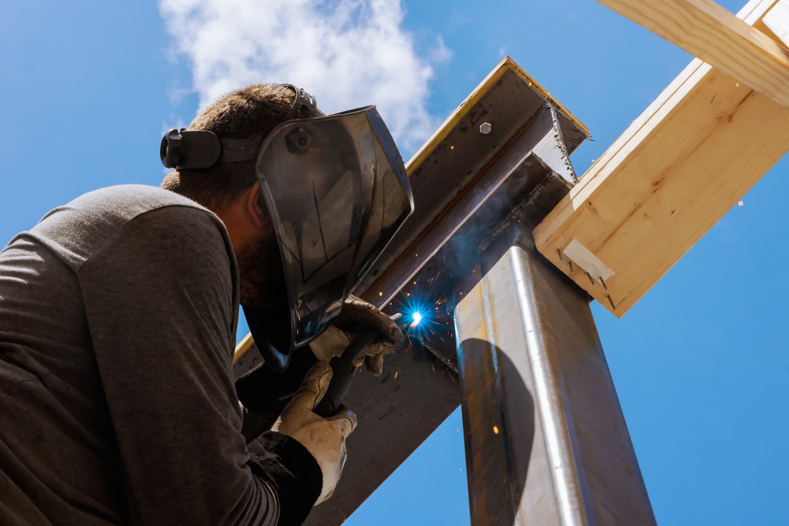 Welder joining a steel beam into a timber roof frame under open sky