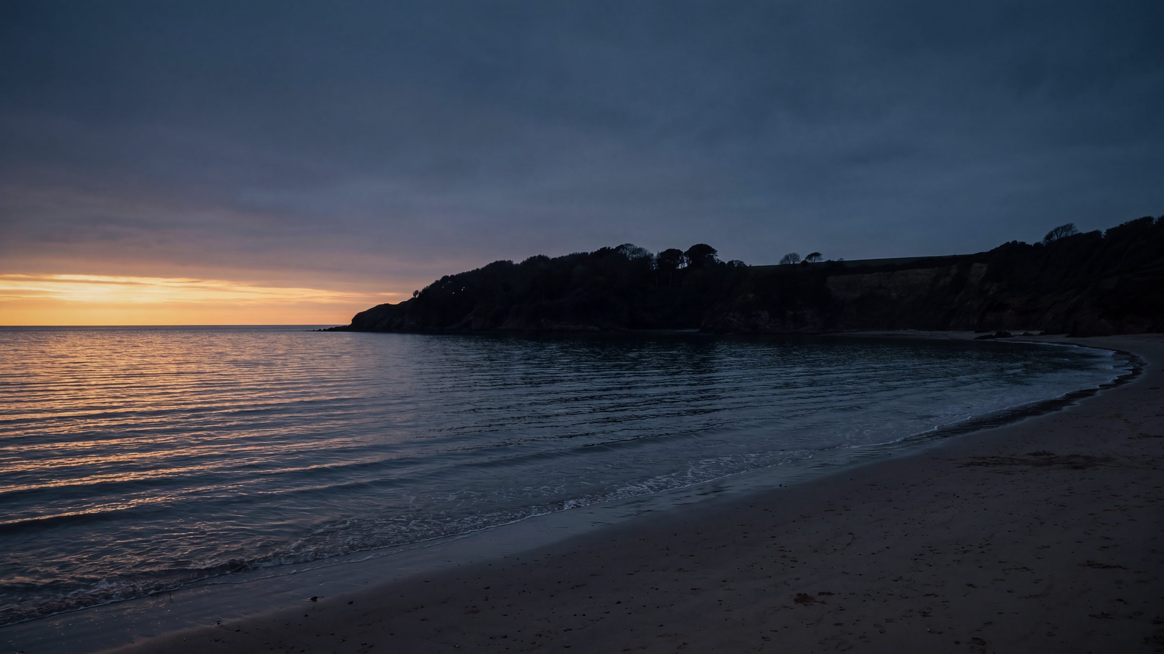 A quiet bay and wooded headland at dusk