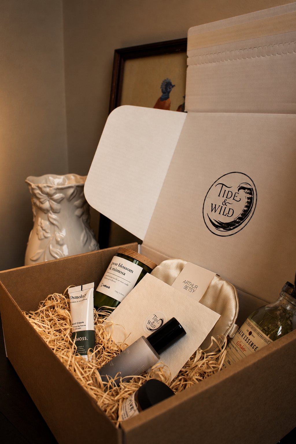 An open Tide & Wild box nestled in straw, with a pear blossom and mimosa candle, silk eye mask, hand cream and amber bath essence