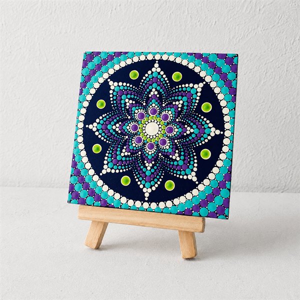 Un cuadro chico sobre un caballete, con un mandala en puntillismo sobre fondo azul oscuro