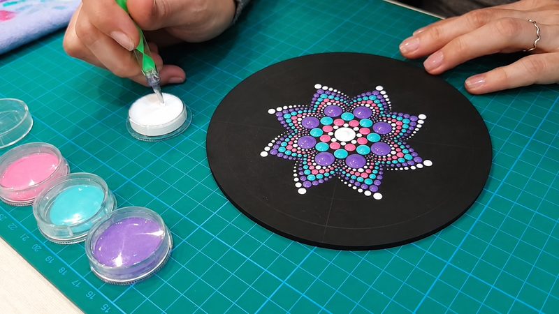 Alejandra cargando pintura en la herramienta, junto al mandala a medio pintar