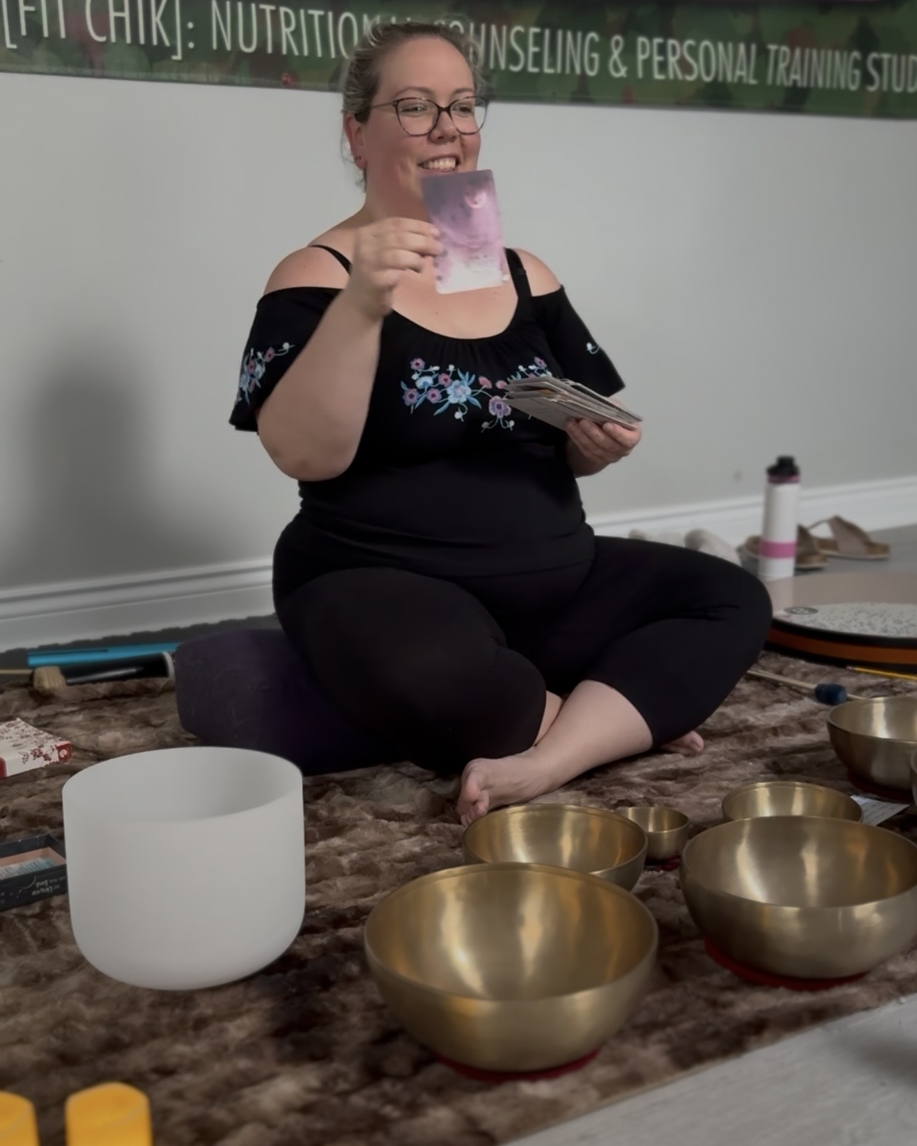 Karolina Autumn sitting amongst sound healing instruments: tibetan bowls, crystal bowl; holding oracle cards by Gabrielle Bernstein The Universe Has Your Back and specifically the card that says "There is nothing sexier than my authentic truth