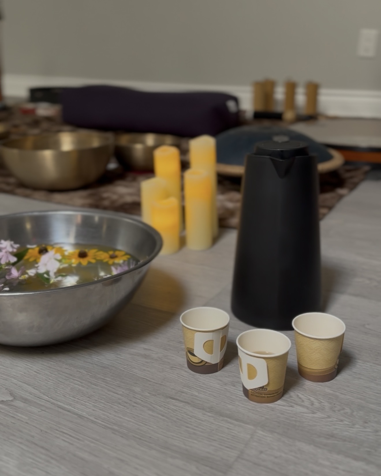 Metal bowl with flowers floating in water, beside a carafe and LED candles