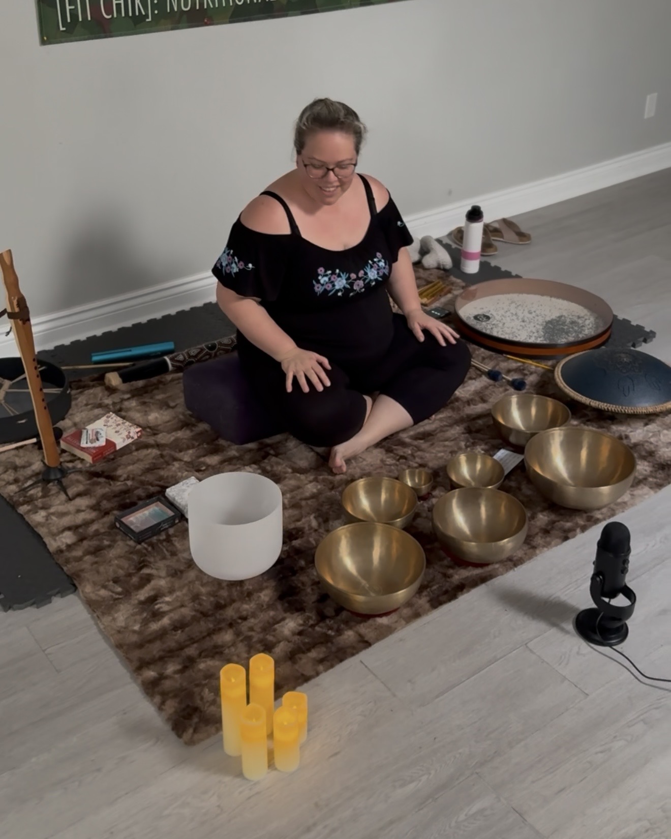 Karolina Autumn sitting amongst sound healing instruments: tibetan bowls, crystal bowl, ocean drum, tongue drum, cedar flute; with a microphone and LED candles