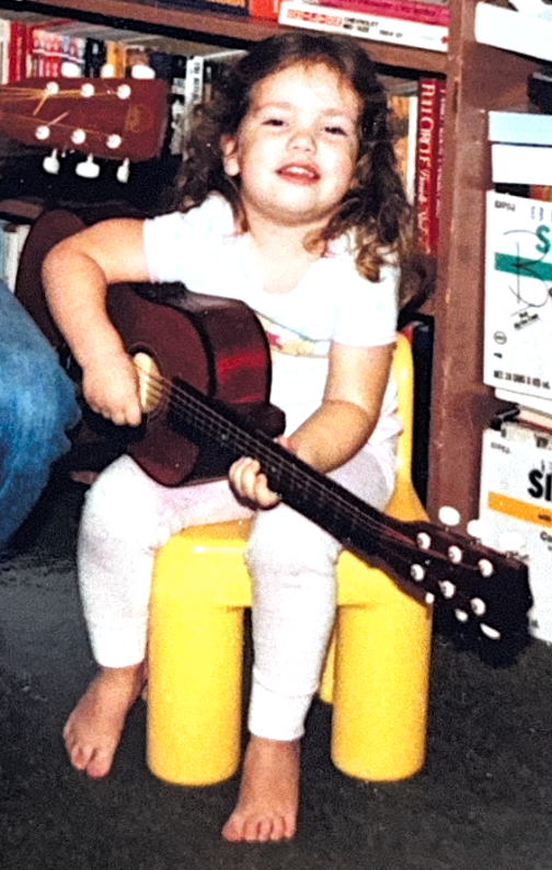 Karolina as a child sitting with a guitar