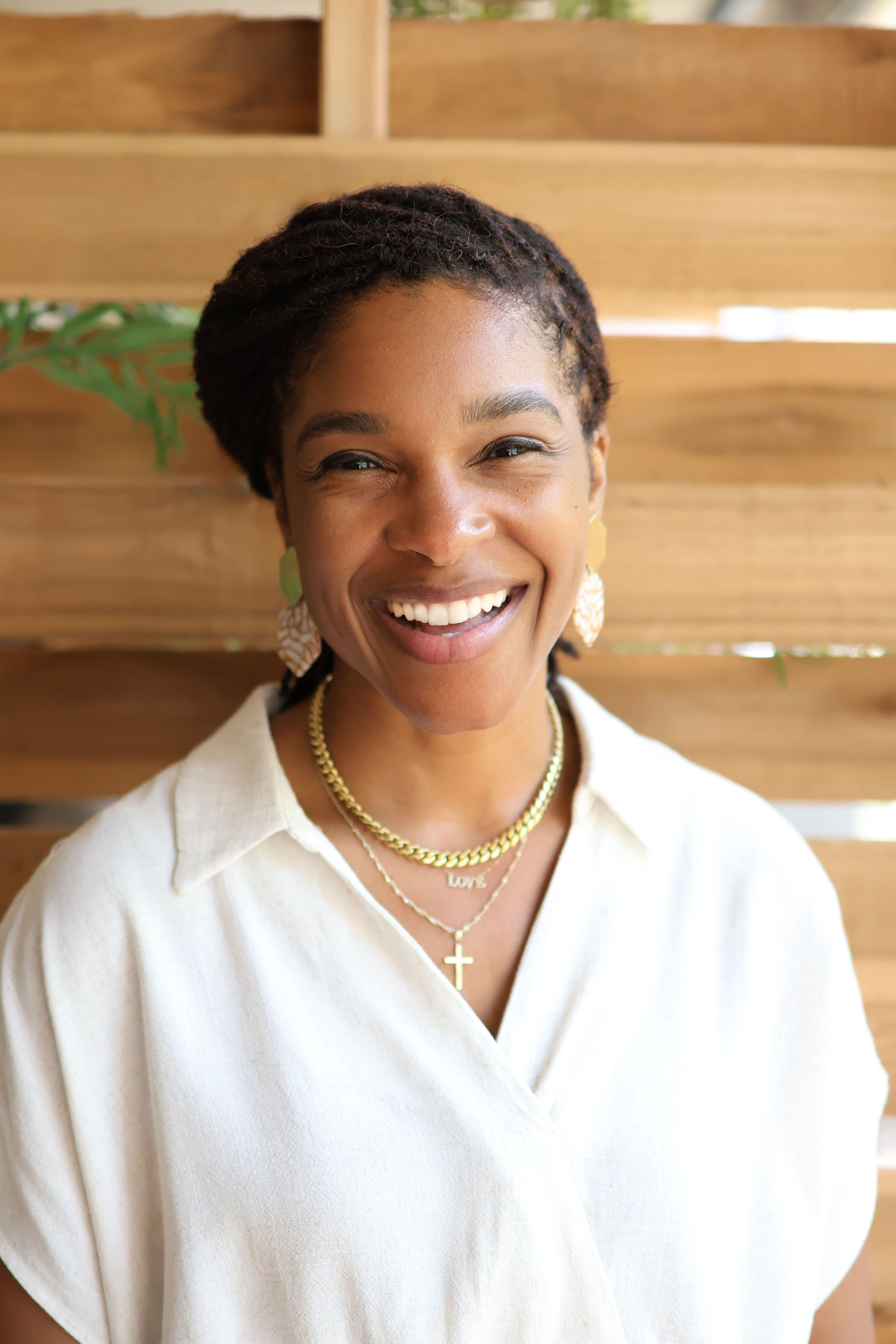 LaKeisha Reid keynote speaker Dallas, standing naturally and laughing in front of a light wooden wall with greenery