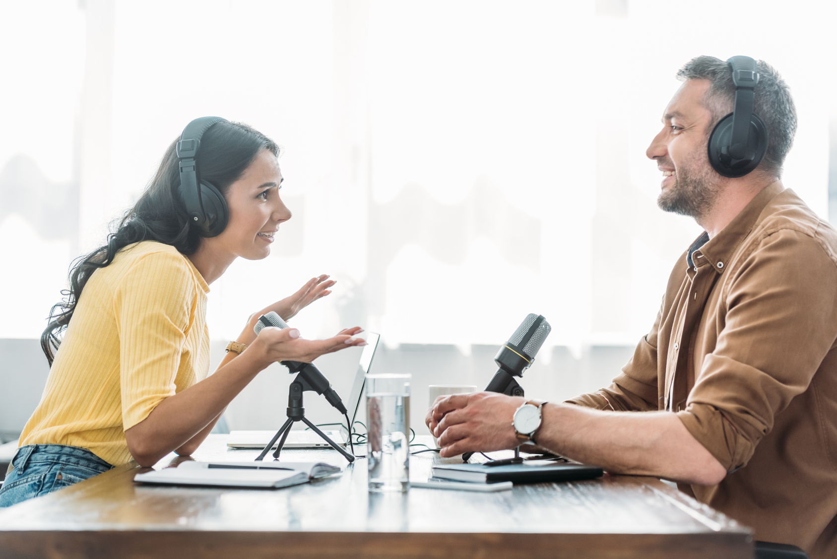 Two podcast presenters speaking across a table with microphones.
