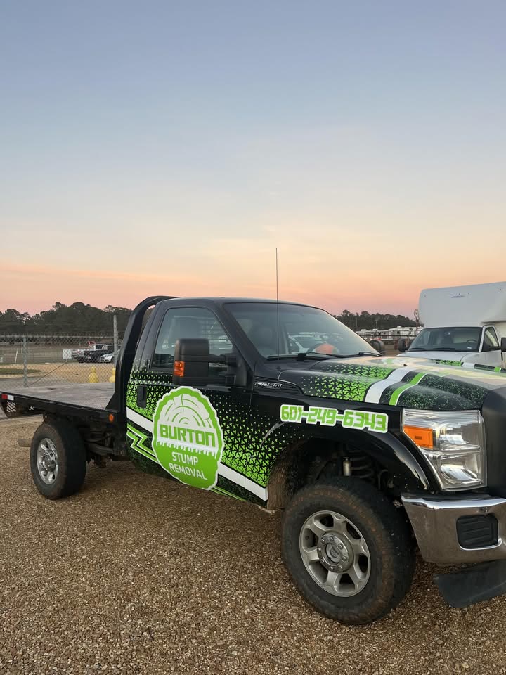 The Burton Stump Removal flatbed truck with its green logo wrap parked at dusk