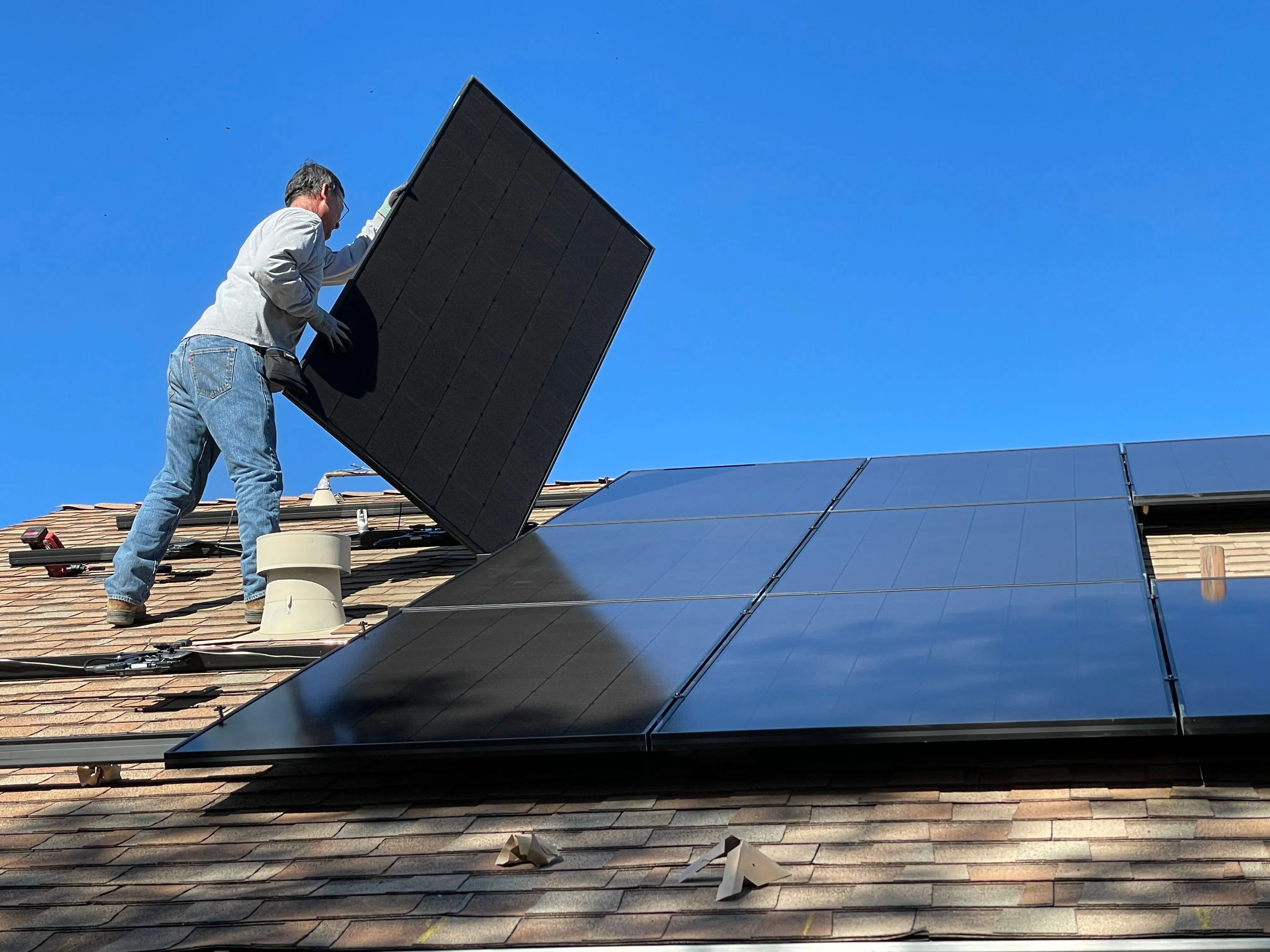 Installer carrying a solar panel across a rooftop