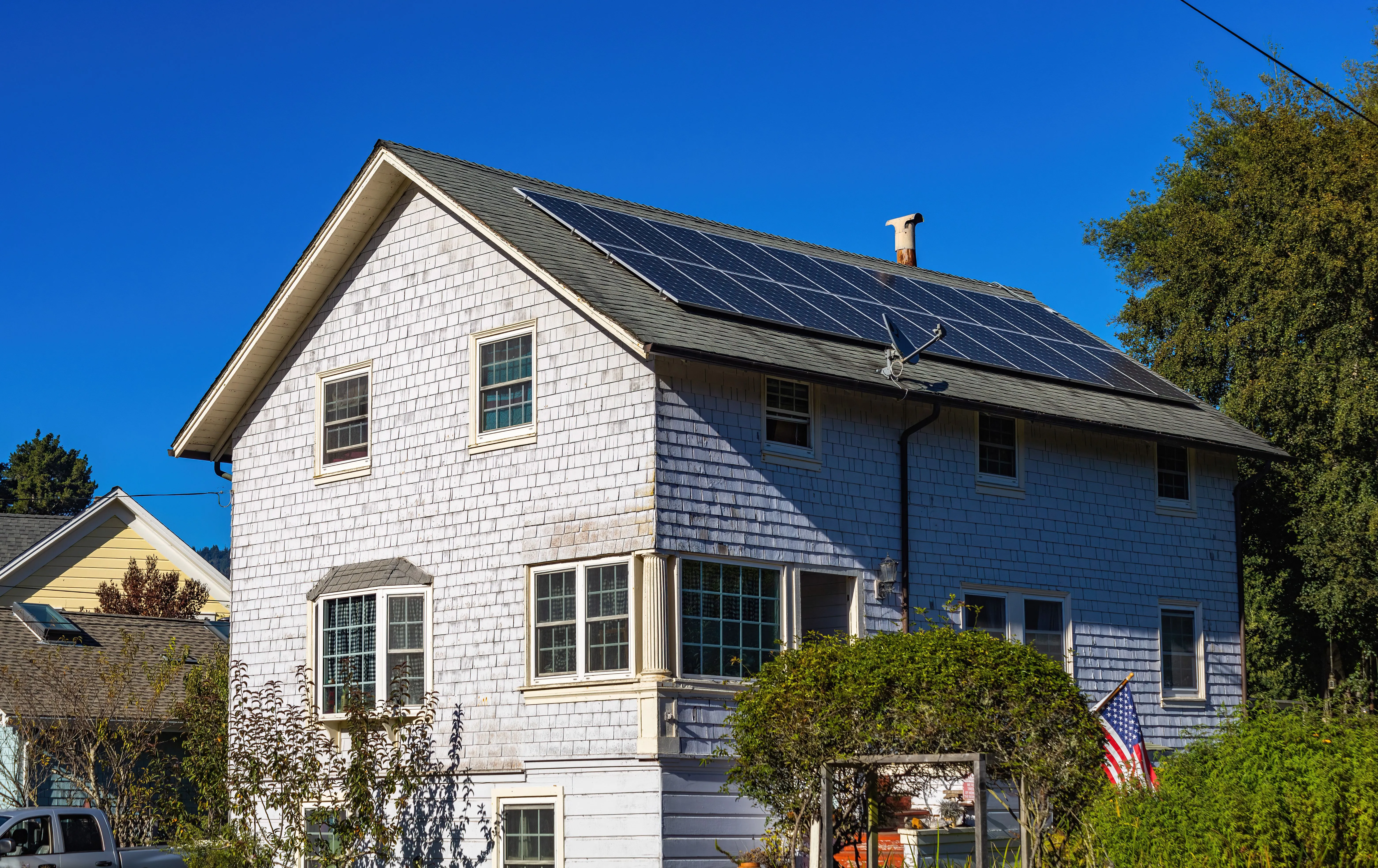 Shingle-sided home with rooftop solar panels under a clear blue sky