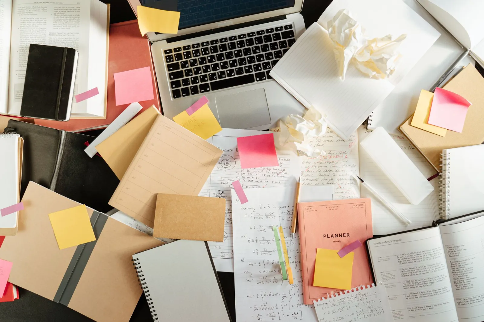 A desk buried in papers, notebooks and sticky notes