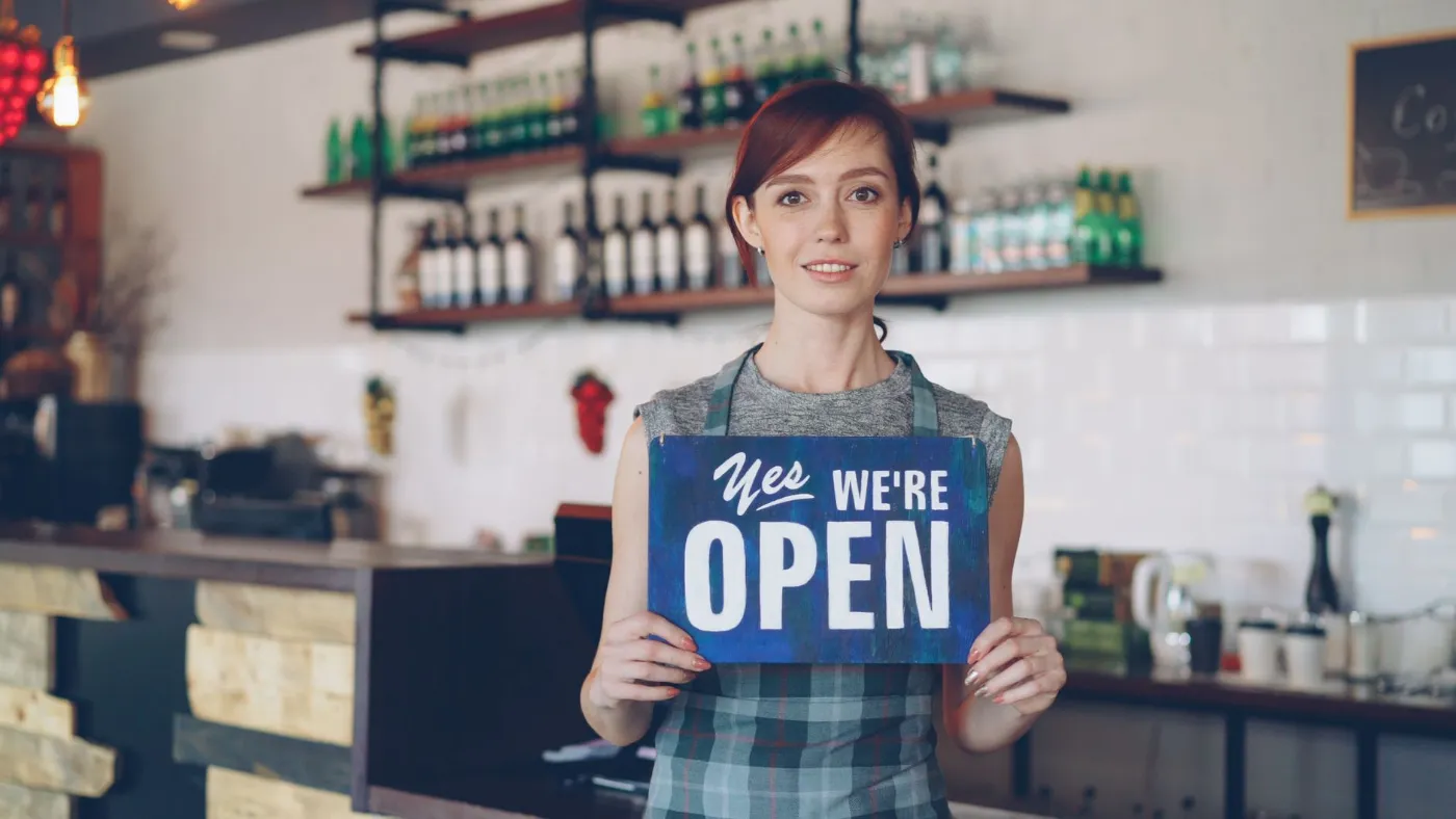 A café owner holding a "We're open" sign