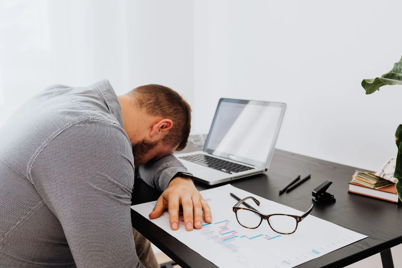 A man slumped over his desk next to his laptop, worn out