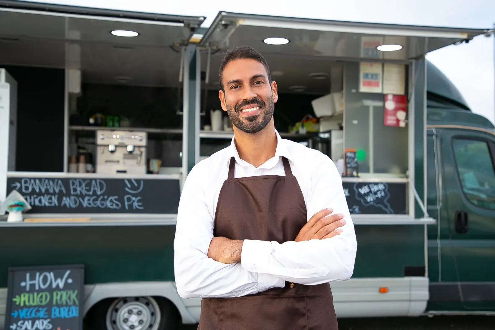 A confident food truck owner standing in front of her truck with her arms crossed