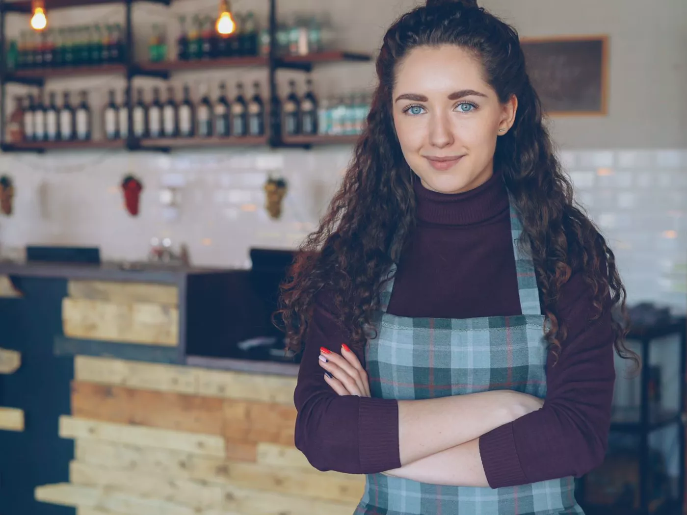 Confident café owner stands with arms crossed inside a rustic, cozy coffee shop.