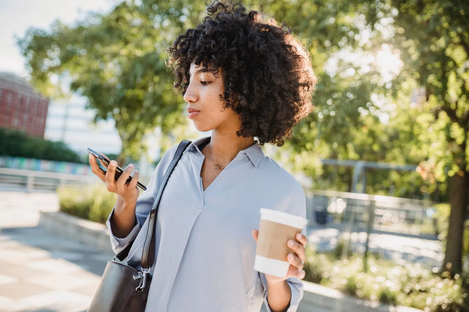A woman checking her phone on the go with a coffee
