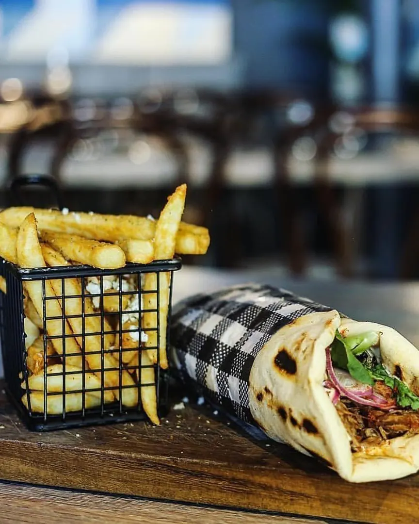 Lamb gyros wrapped in pita with a basket of chips topped with feta