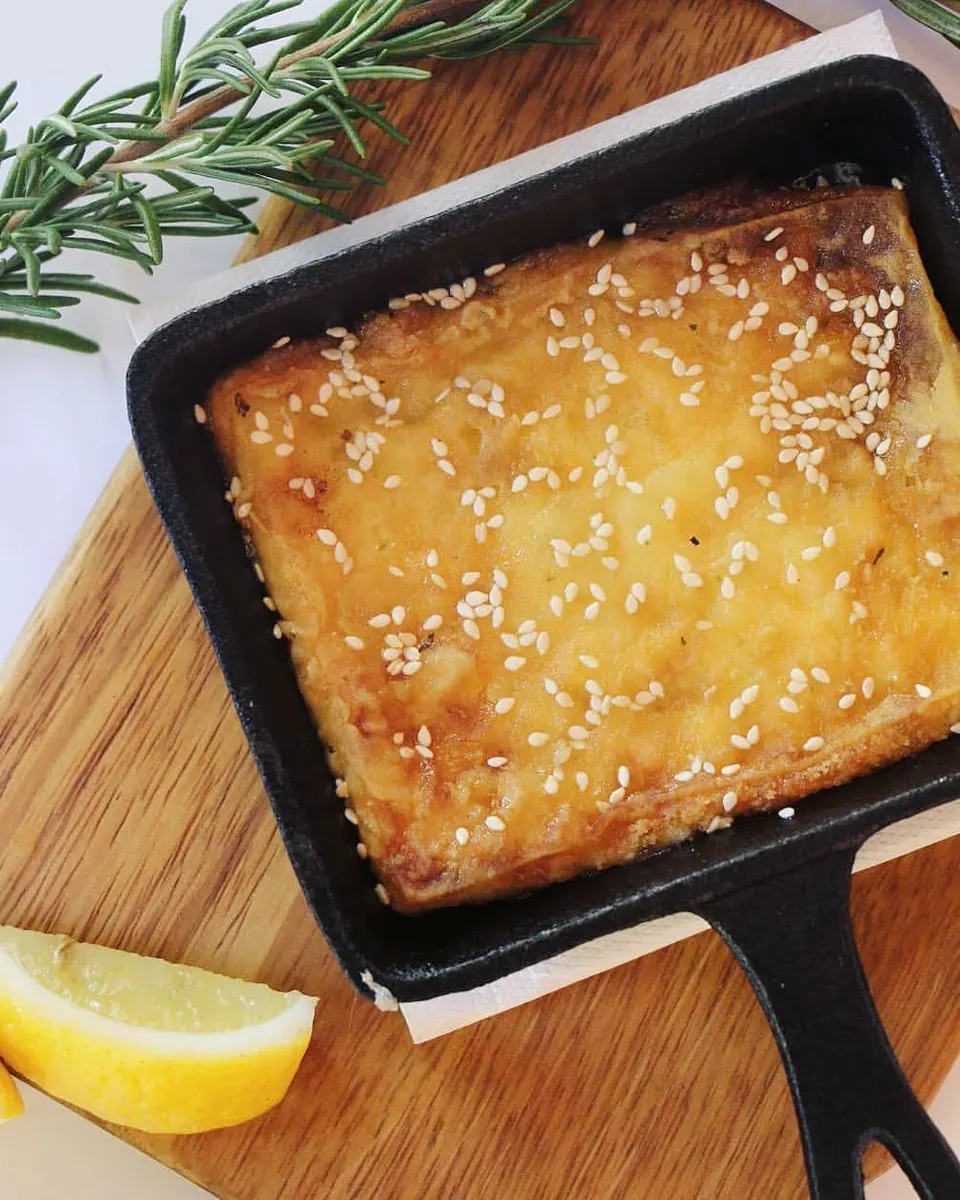 Saganaki cheese baked with honey and sesame in a cast-iron pan, with lemon
