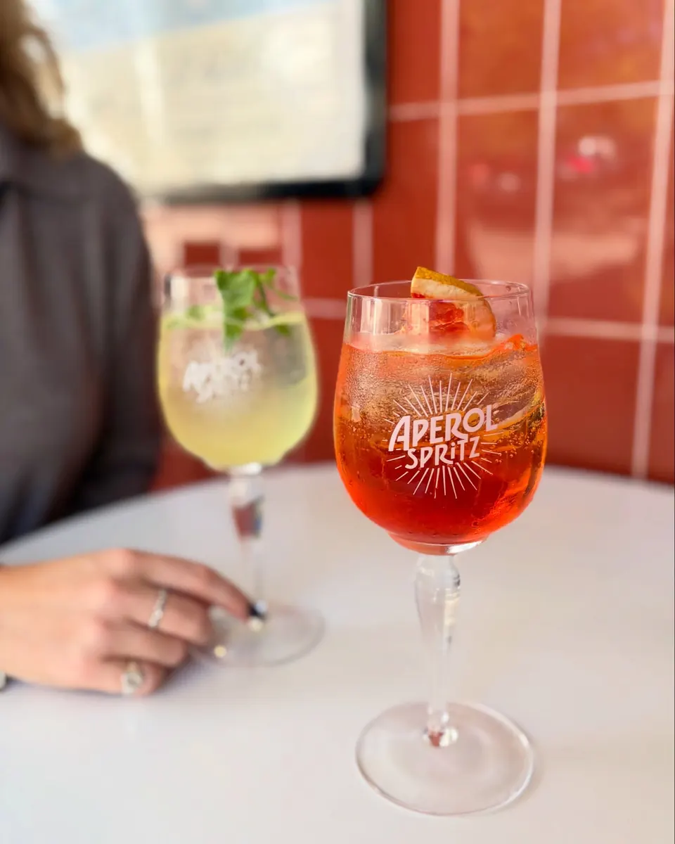 An Aperol spritz and a gin cocktail on a marble table against red tiles