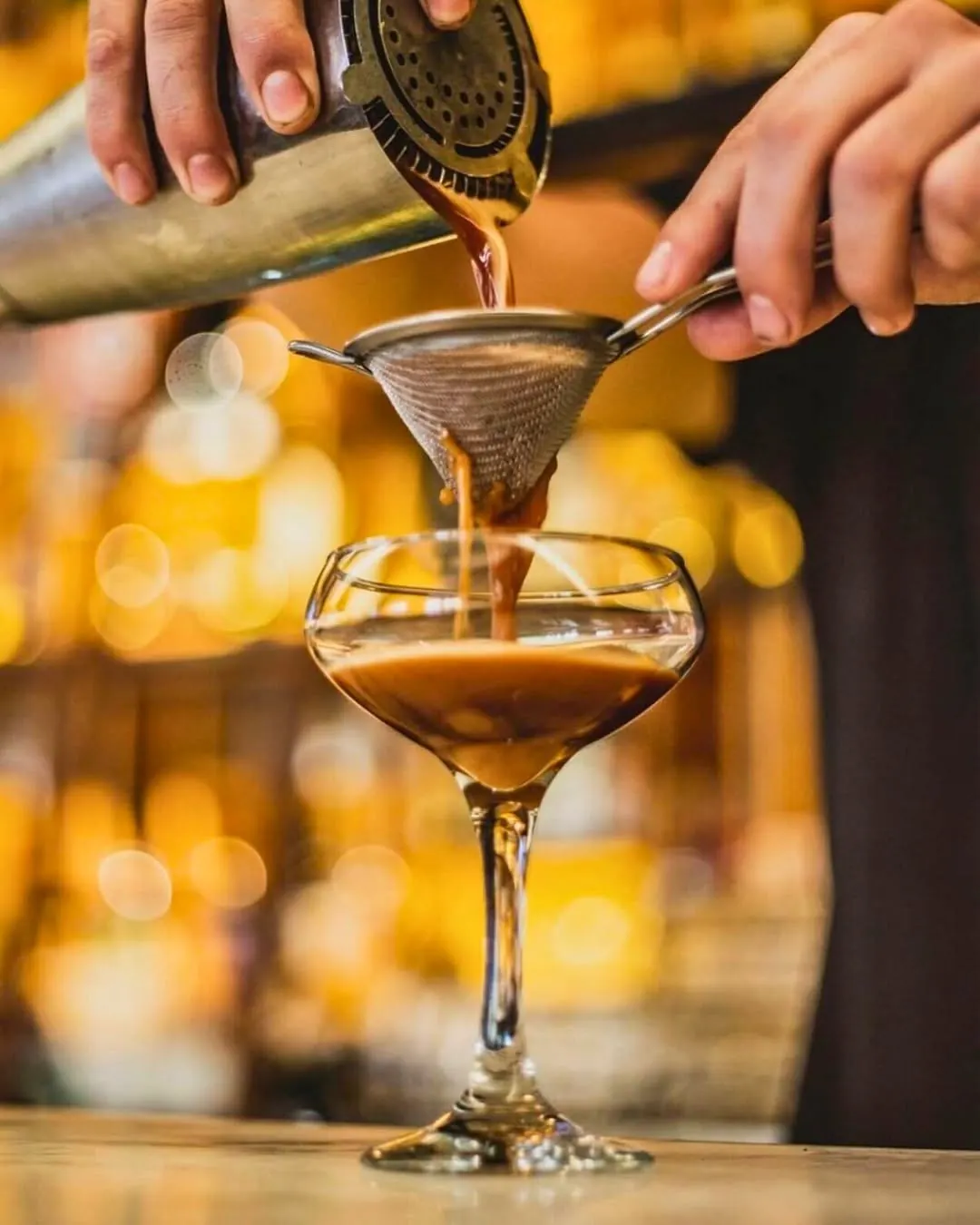 An espresso martini being strained into a coupe at the bar