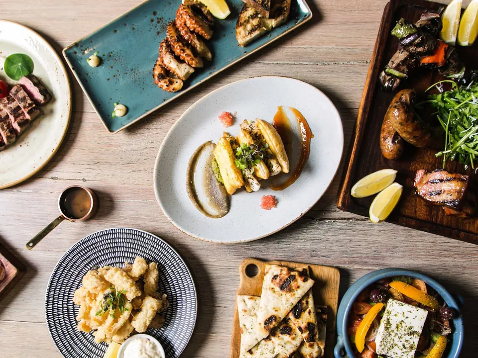 An overhead spread of Greek share plates, grilled meats and dips