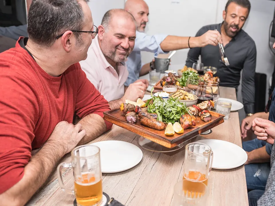 Friends sharing a Greek feast board and beers around a long table
