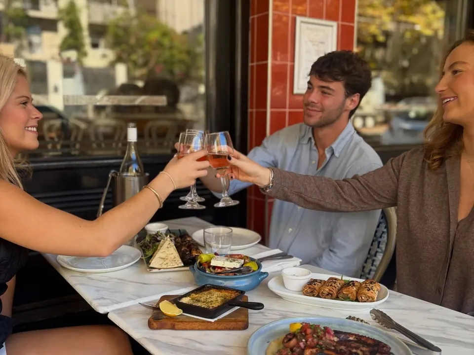 Friends toasting with rosé over shared Greek plates at a window table at The Phoenix Woollahra