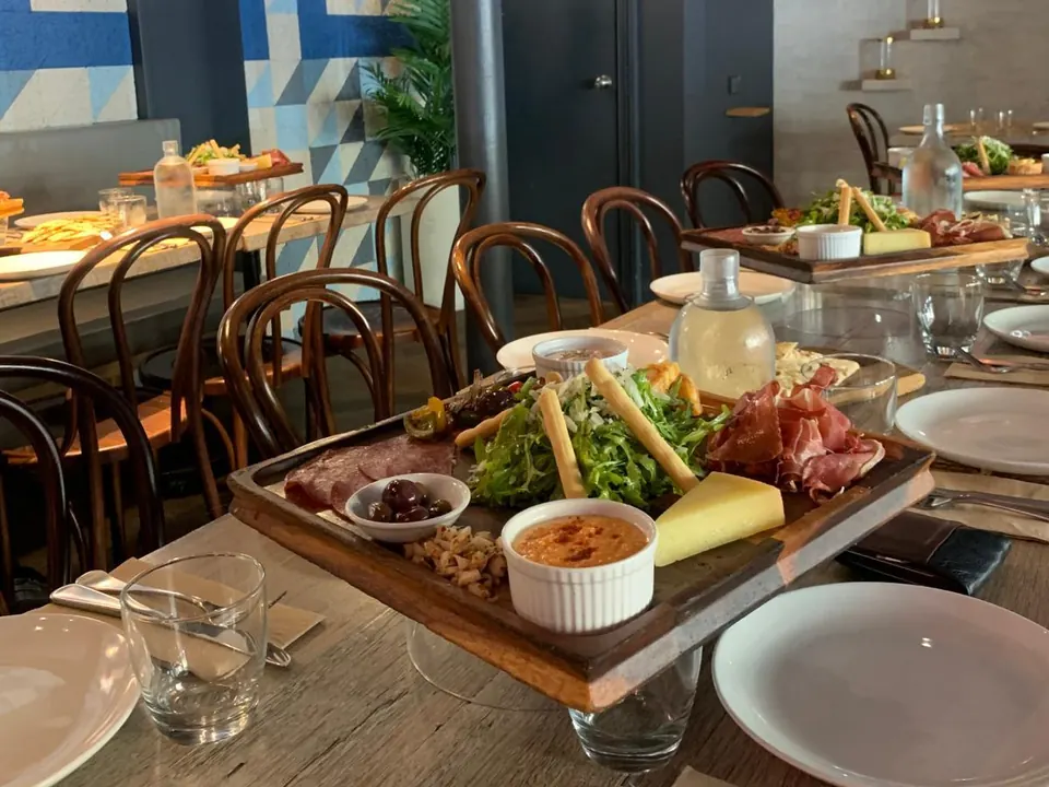 A long lunch table with a share board beneath the Greek-key mural in The Nest